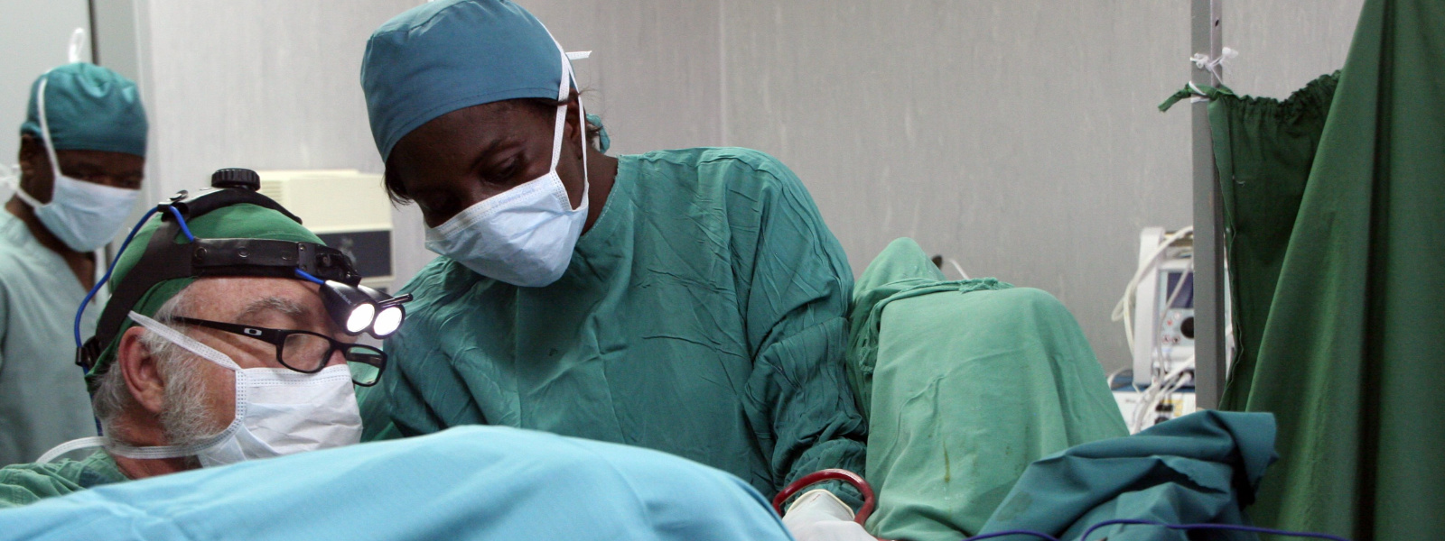 Surgeon in scrubs performing fistula surgery with nurse attending
